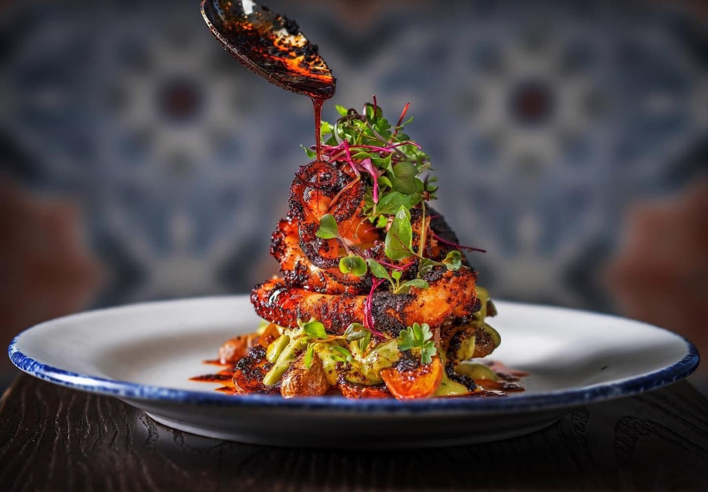 Grilled food stacked on a plate with salsa macha being spooned over the top.